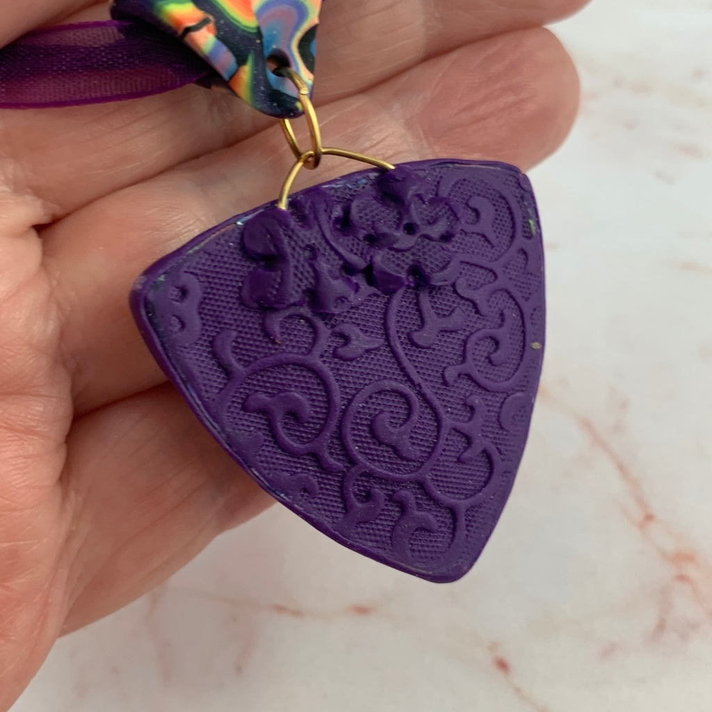 Back view of handmade triangular pendant held in hand showing textured artisan finish.