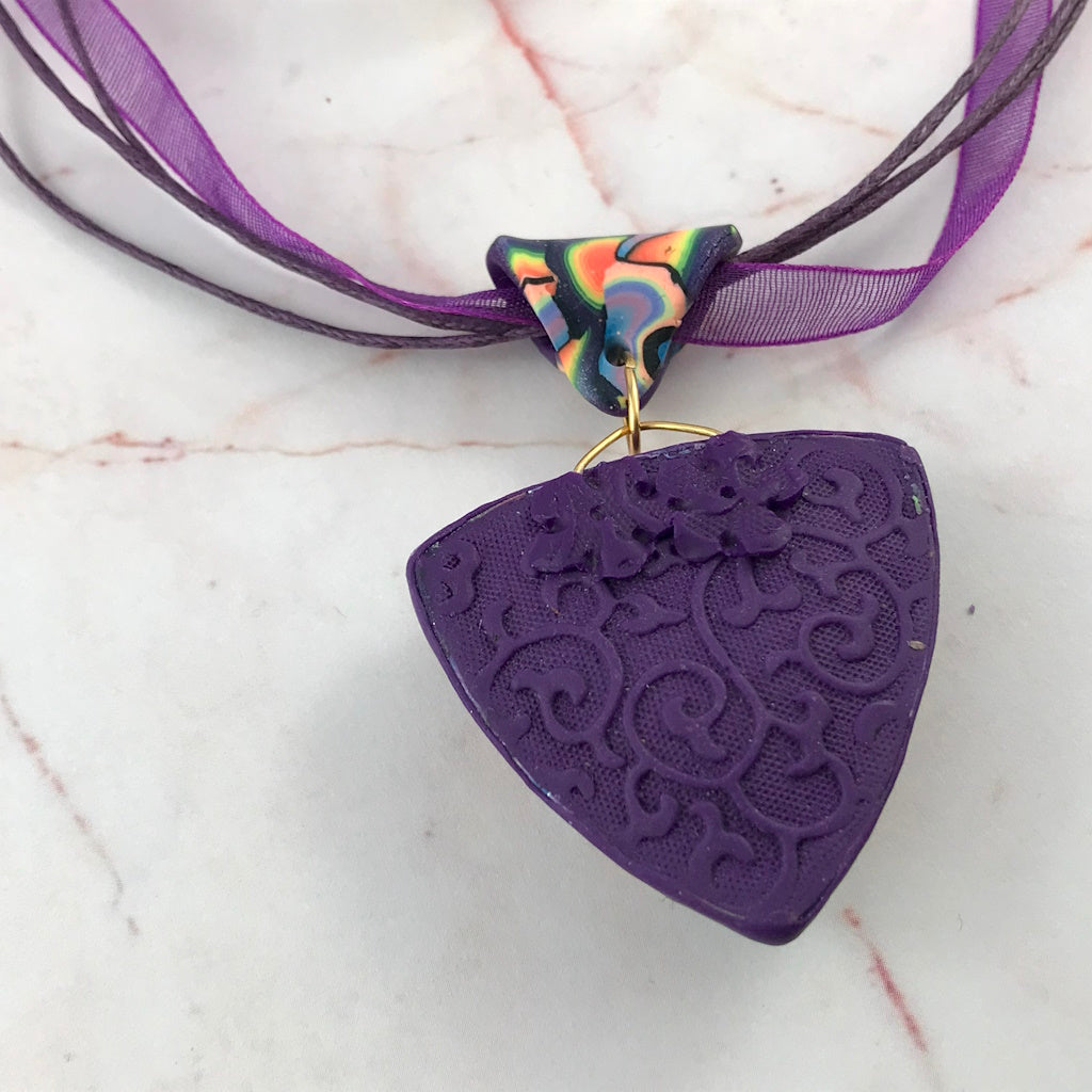 Back view of handmade triangular pendant necklace showing textured purple artisan finish.