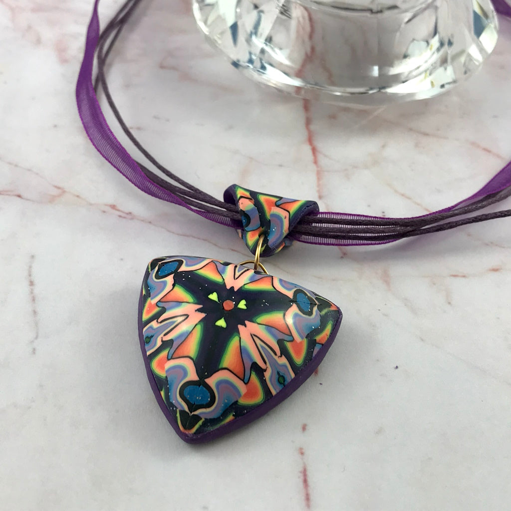 Styled front view of handmade triangular pendant necklace with purple cord and multicolour pattern.