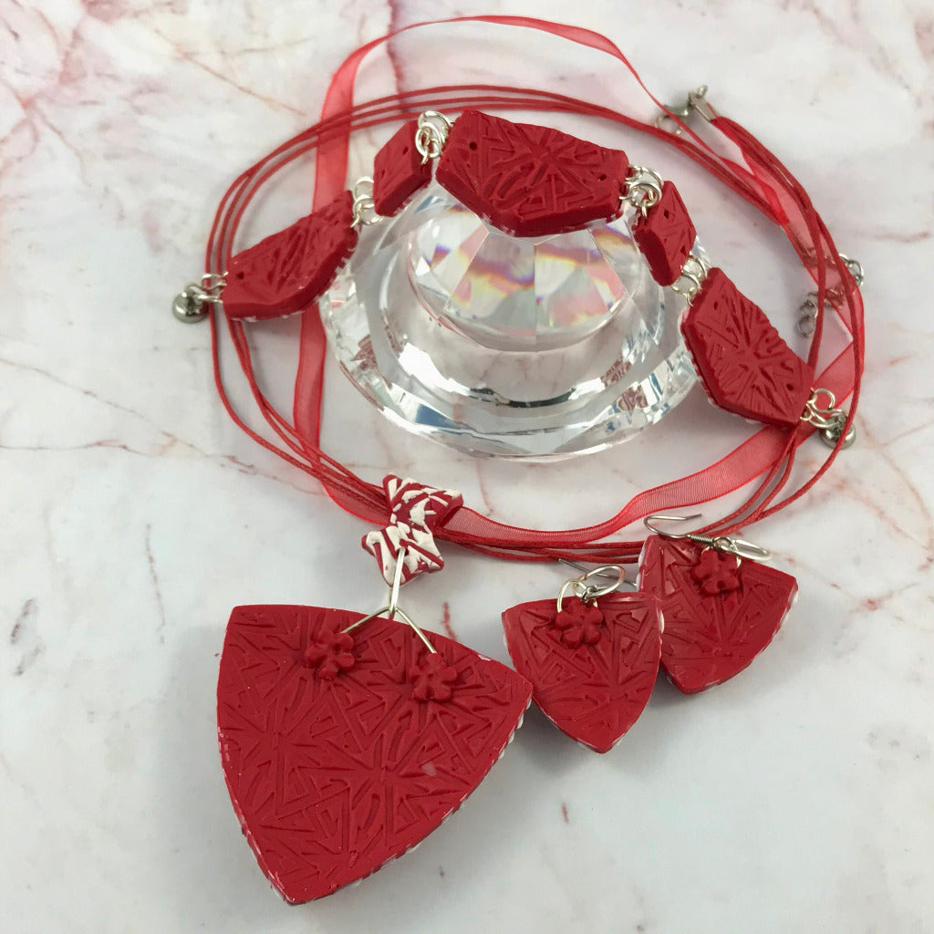 Back view of red and white handmade polymer clay pendant, earrings, and bracelet set showing finished patterned reverse side.