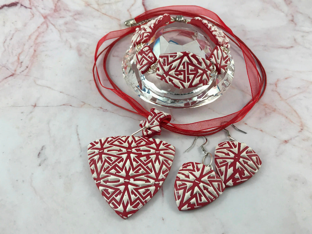 Handmade red and white textured polymer clay jewellery set featuring pendant necklace, matching earrings, and bracelet displayed on glass stand.
