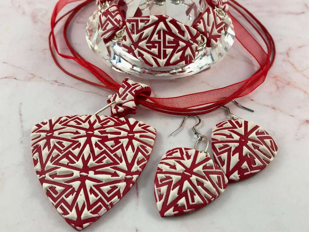 Close-up detail of red and white textured polymer clay pendant, matching earrings, and bracelet with raised geometric pattern.