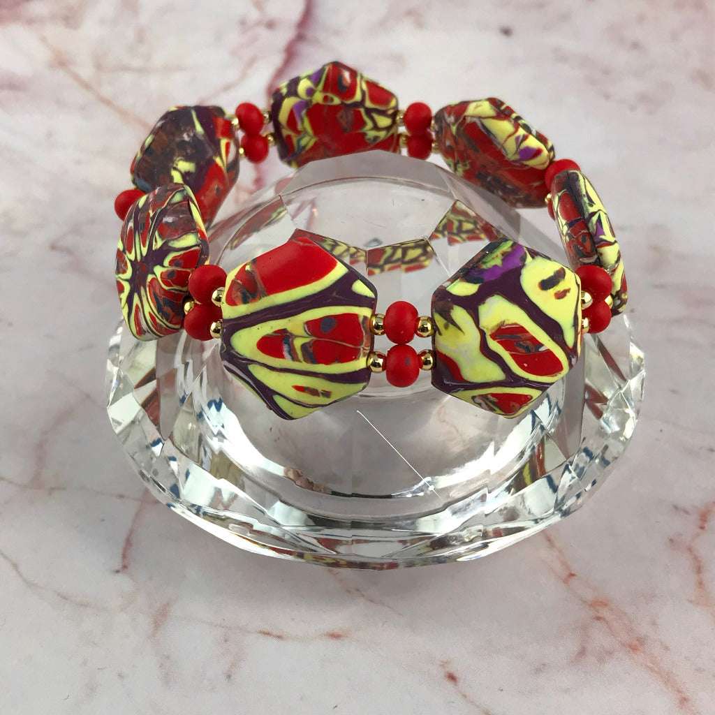 Close-up side view of handmade red and yellow stretch bracelet with unique marbled statement beads