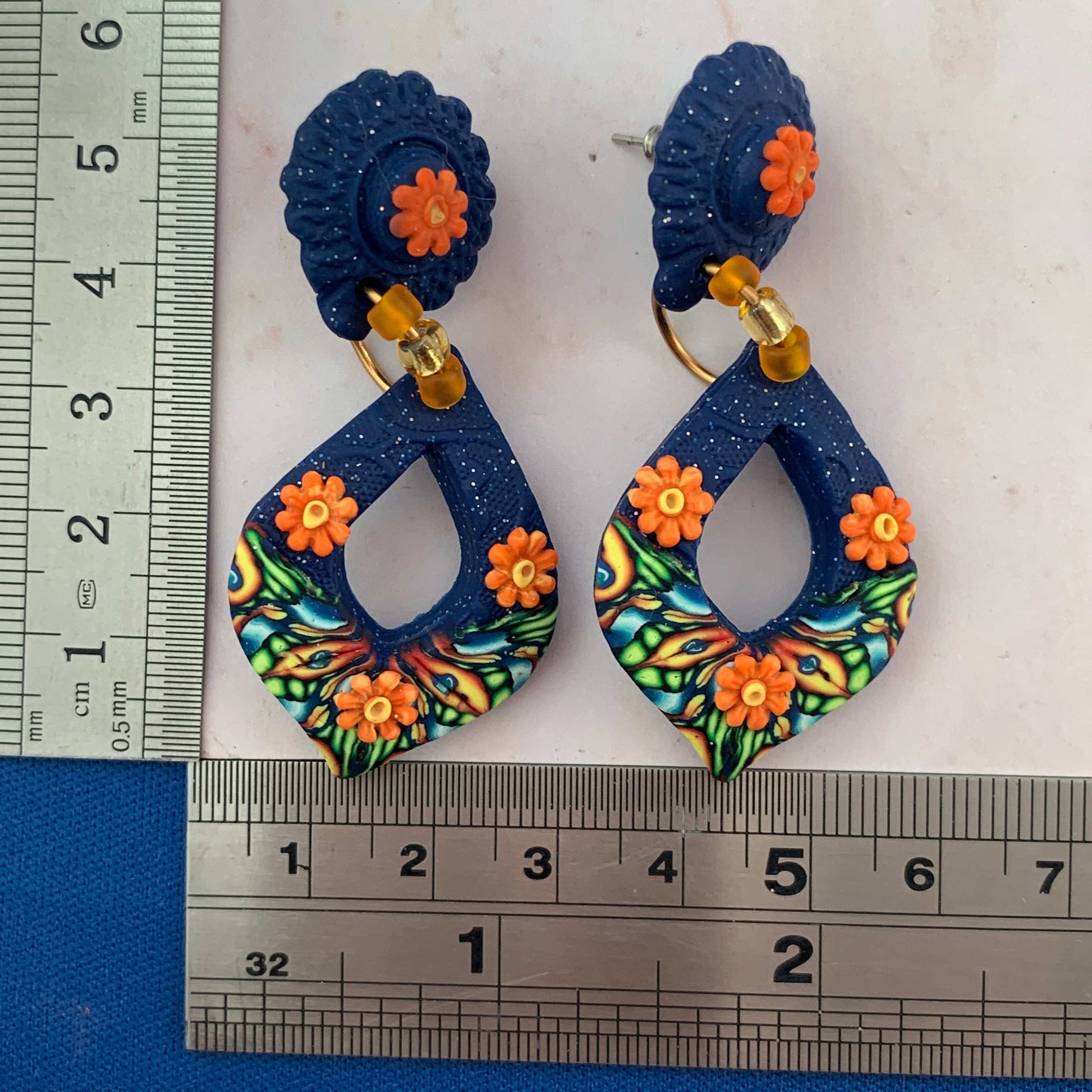 Award-winning Rennique hand-sculpted blue and orange teardrop fashion earrings shown with ruler size guide for pierced ears.
