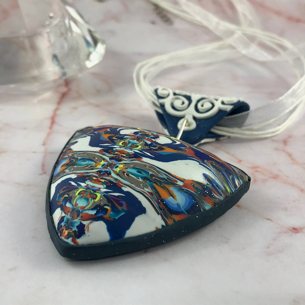 Side view of bold blue and white polymer clay pendant highlighting curved air-filled shape.