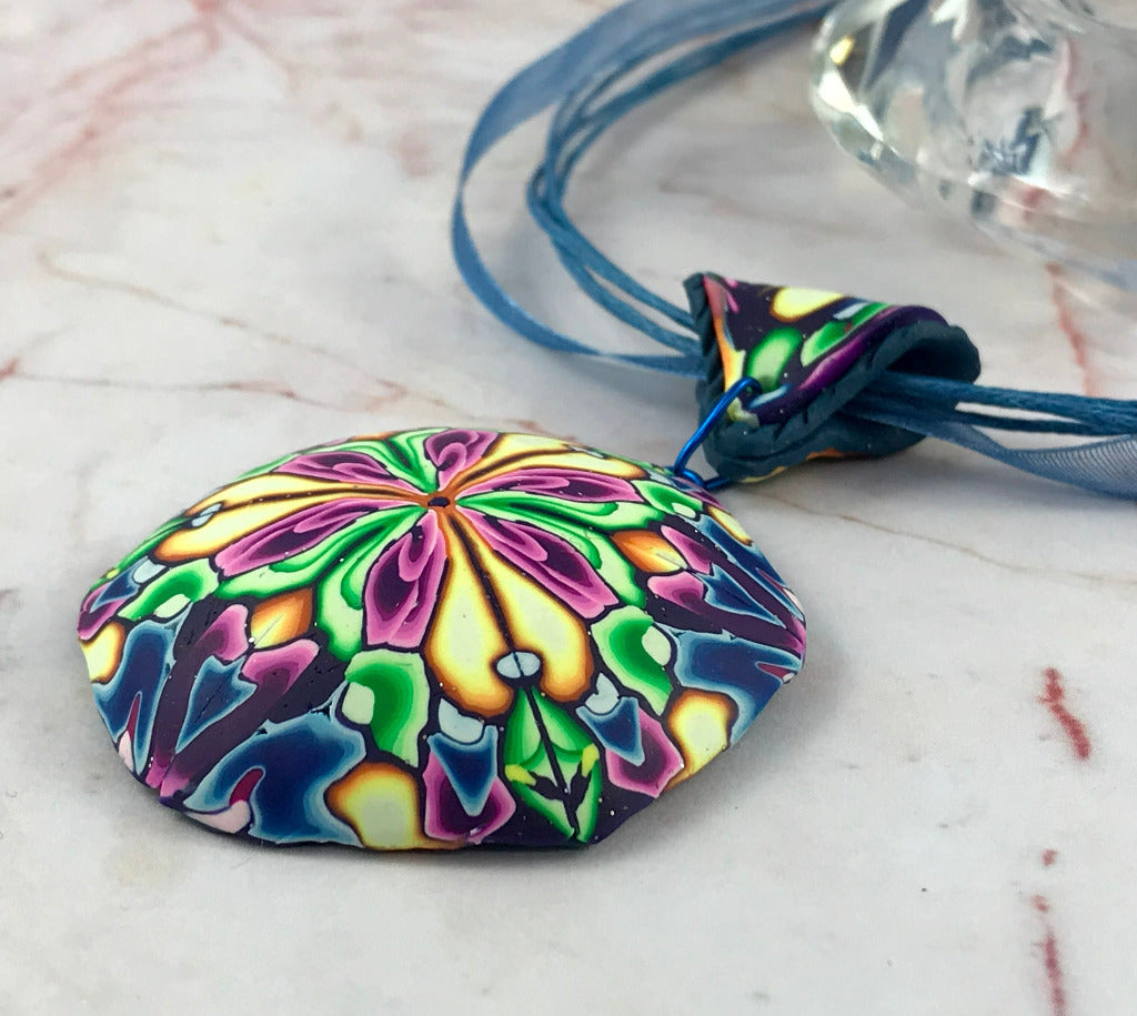 Rennique bold floral hanging pendant necklace displayed on blue ribbon cord with vibrant floral polymer clay pattern