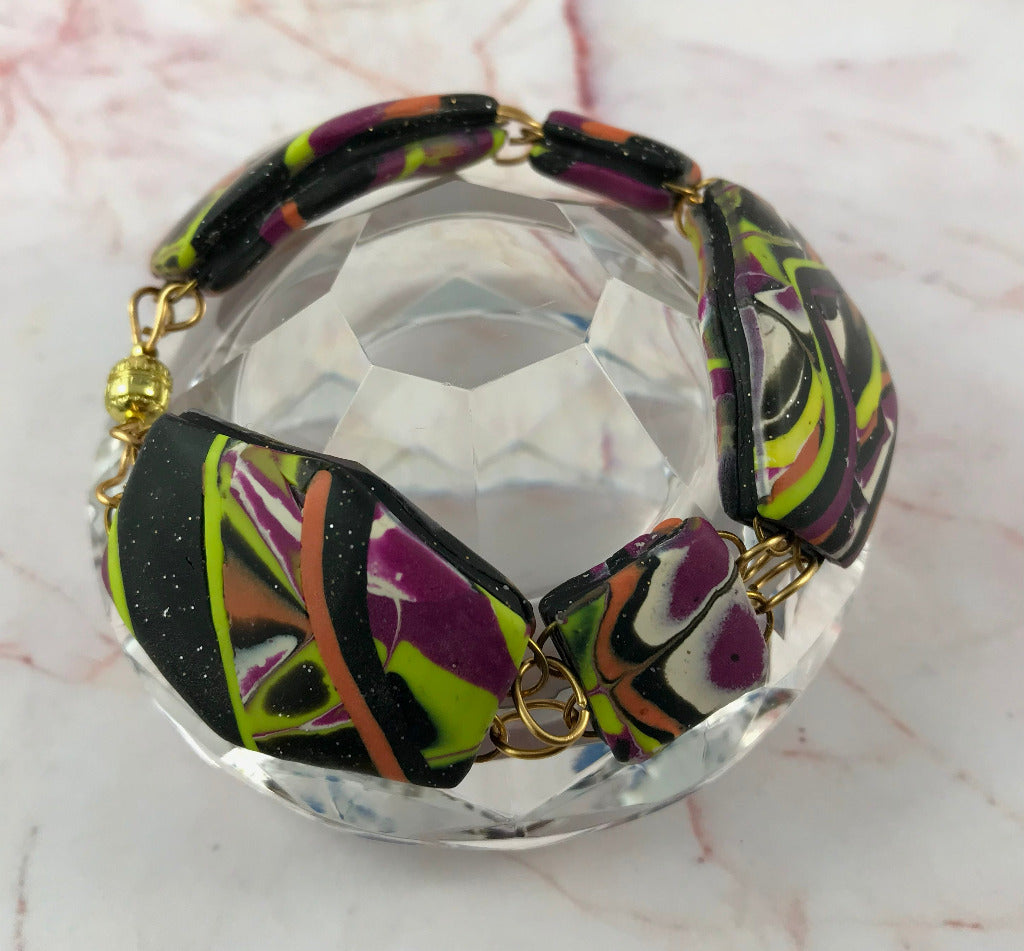 Abstract handmade bracelet displayed open to show clasp, shape, and bold patchwork pattern.