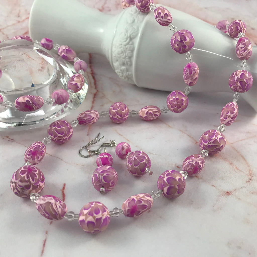 Styled image of pink flower necklace, earrings, and bracelet set with graduated floral beads.