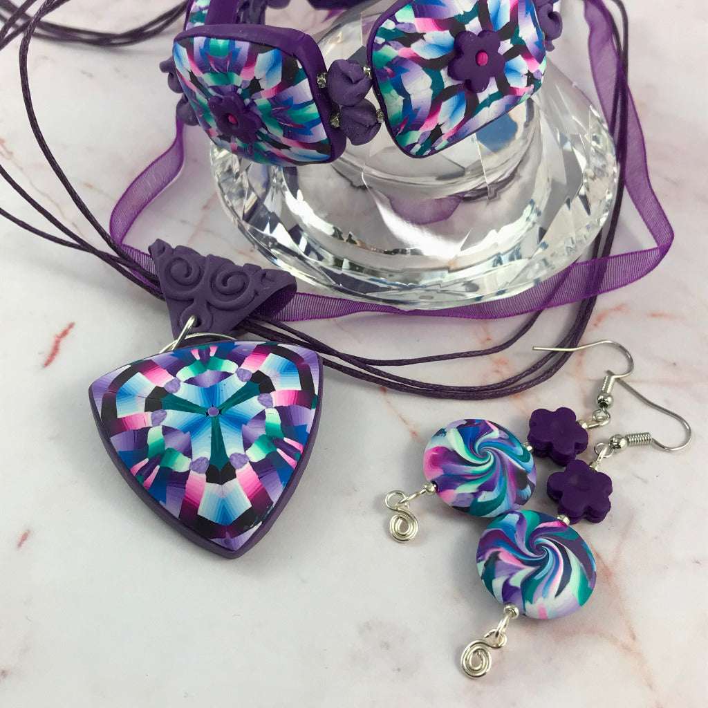 Flat lay close-up of pink and purple geometric jewellery set with pendant, earrings, and bracelet.