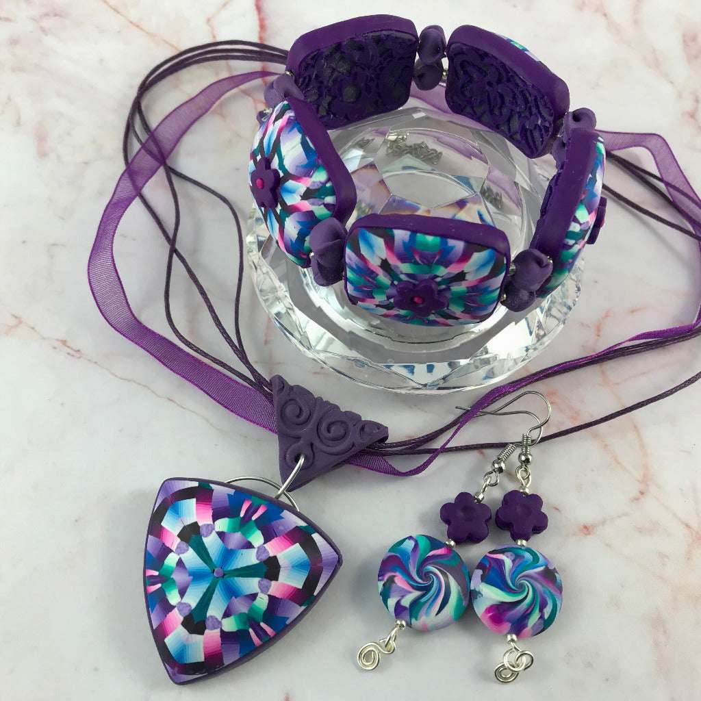Side view of handmade pink and purple polymer clay pendant, bracelet, and earrings set showing curved profile.