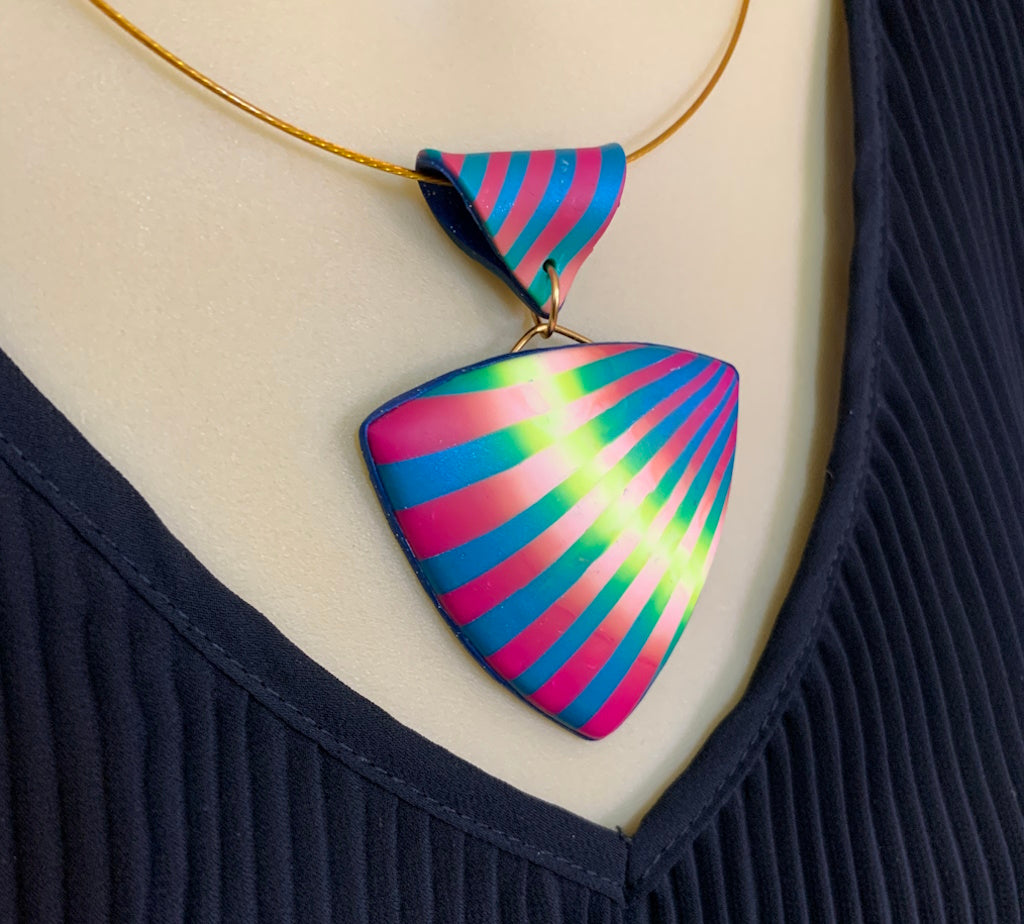 Rennique handmade statement pendant necklace worn on mannequin, featuring bold pink, teal, and neon lime striped polymer clay design on sheer ribbon cord.