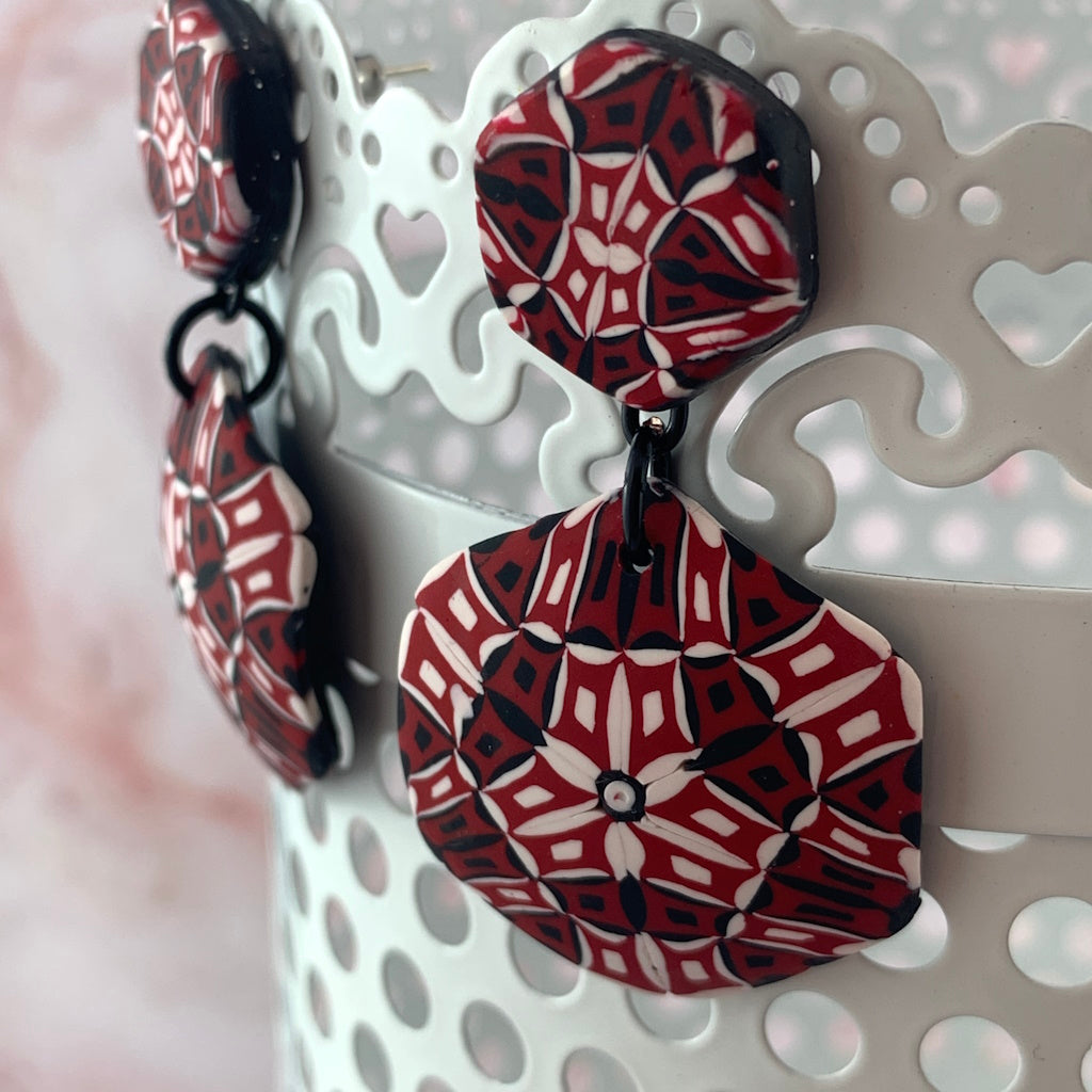 Close-up of Rennique designer polymer clay statement earrings in red, black and white kaleidoscope pattern wearable art style.