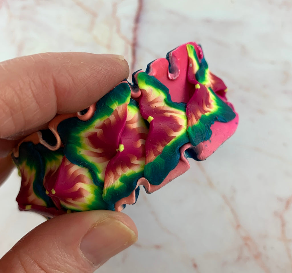 Close-up of Rennique handmade wearable art cuff bracelet featuring sculptural tropical flower petals in vibrant pink, green and blue polymer clay.