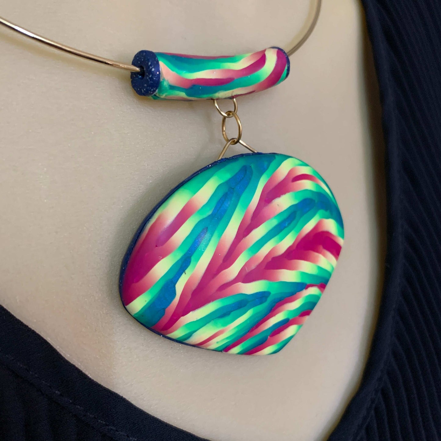 Rennique handmade statement pendant necklace featuring bold pink, teal, aqua and cream striped polymer clay pendant on gold wire choker, displayed on mannequin.