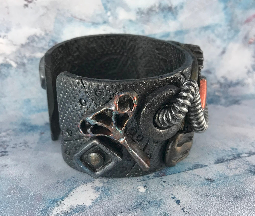 Handcrafted steampunk cuff bracelet by Rennique showcasing key and gear details with textured metallic polymer clay in dark industrial tones.