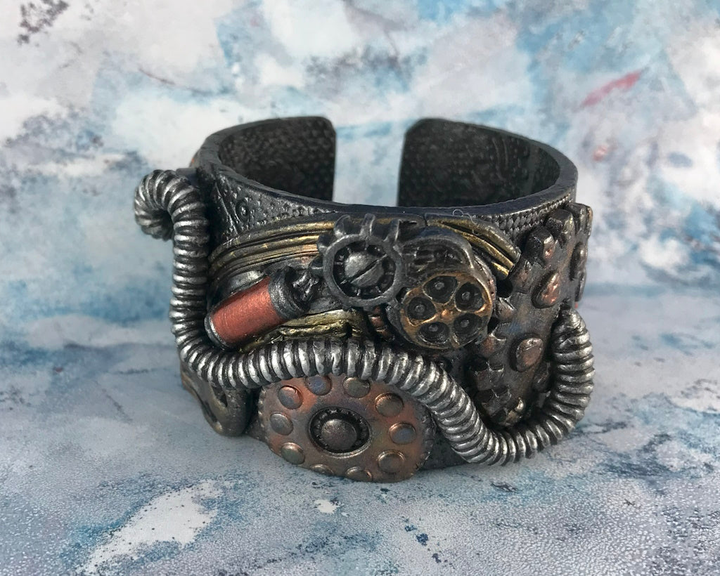 Close-up of textured steampunk cuff bracelet with riveted metal effect, coiled tubing, and industrial design handcrafted from polymer clay.