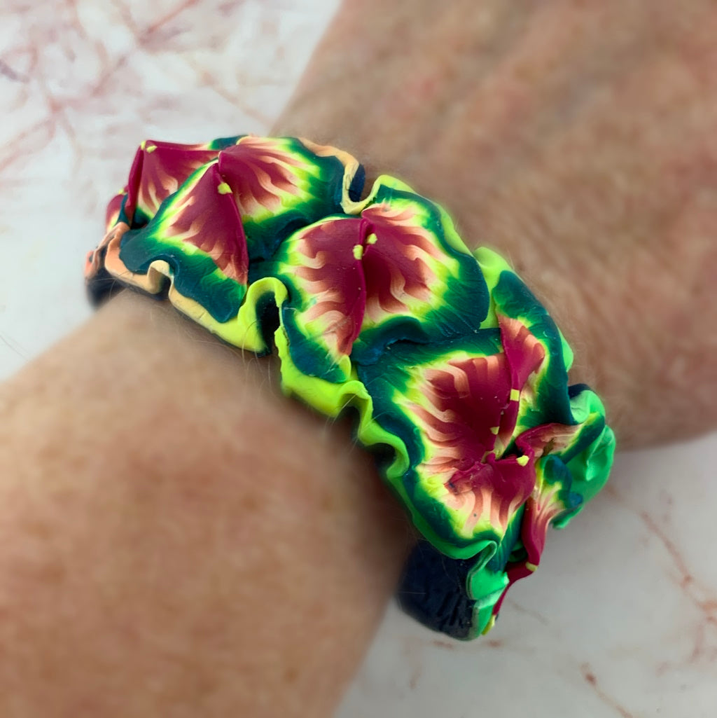 Rennique Studio one-of-a-kind wearable art cuff bracelet in bold tropical floral design with vibrant pink, green and blue handmade polymer clay details worn on wrist.