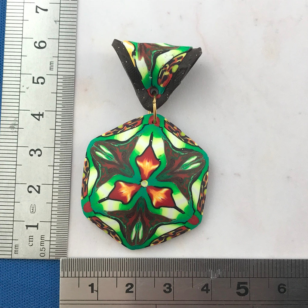 Rennique handcrafted tropical polymer clay pendant with ruler for size reference, featuring hexagon kaleidoscope design in green, black, cream, and orange.