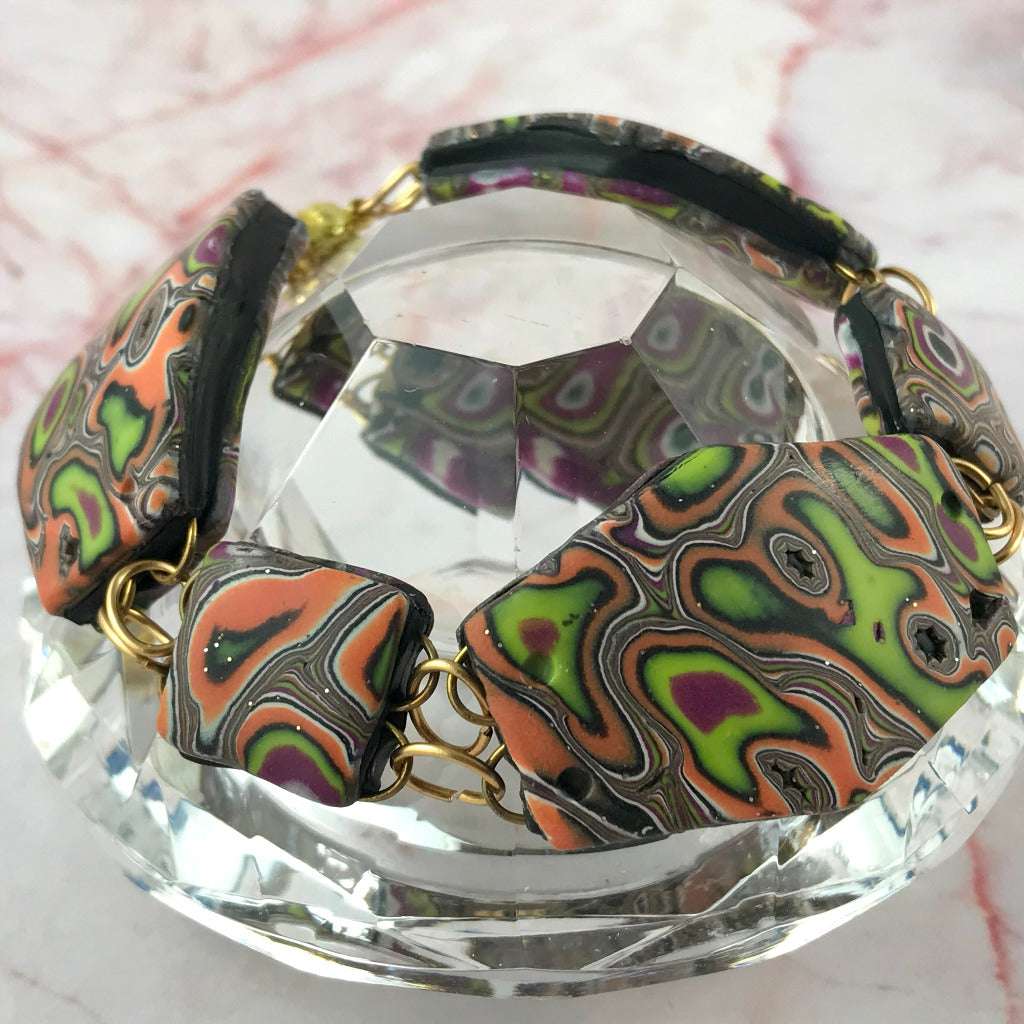 Side angle view of handcrafted polymer clay bracelet with ripple autumn swirl pattern in plum, coral, lime green and black tones.