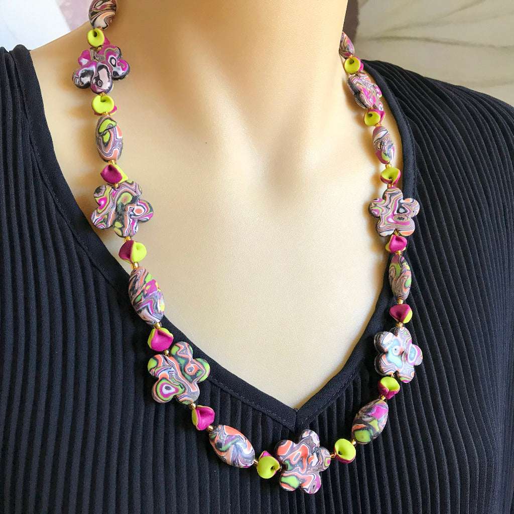 Handmade ripple autumn tone necklace worn on mannequin featuring floral and oval marbled beads in lime green, plum, coral and black.