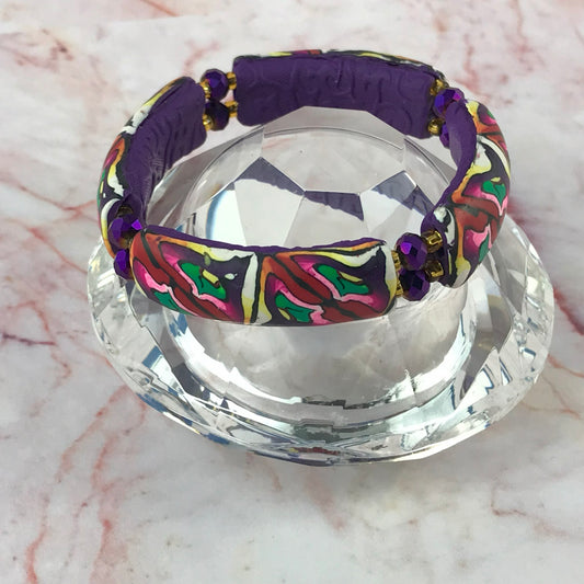 Artisan handmade stretch bracelet displayed on crystal stand with colourful abstract polymer clay beads, plum backing and purple crystal accents.
