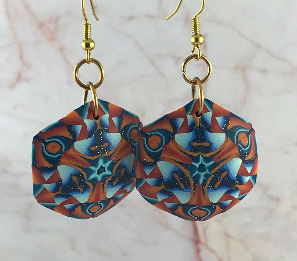 Front view of handmade statement polymer clay earrings with bold mandala geometric pattern in orange, teal, blue and gold hooks.