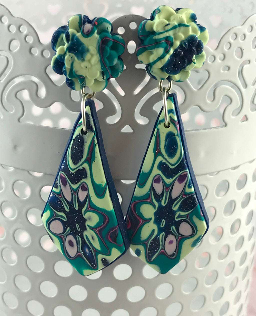 Close-up of handmade teal and navy polymer clay statement earrings featuring abstract floral pattern and drop shape.