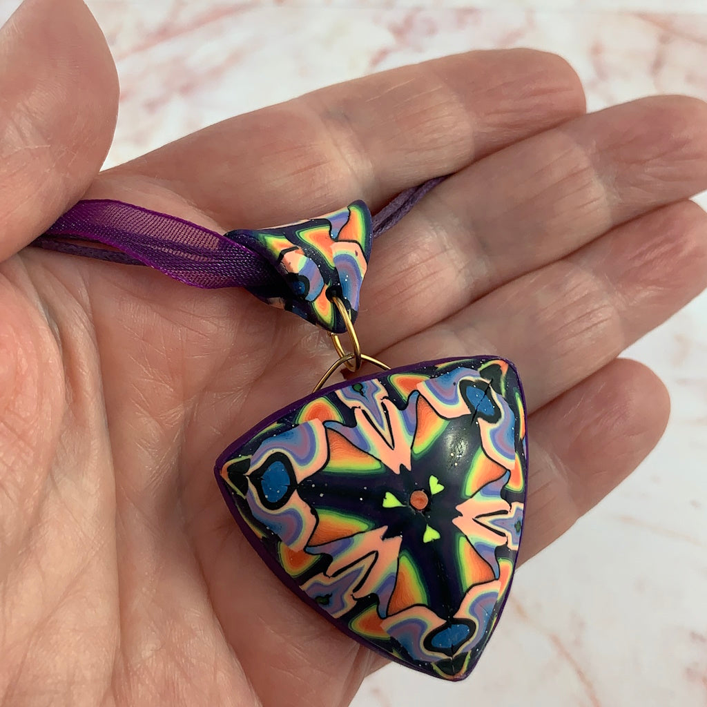 Handheld front view of triangular handmade statement pendant necklace with vibrant multicolour pattern.