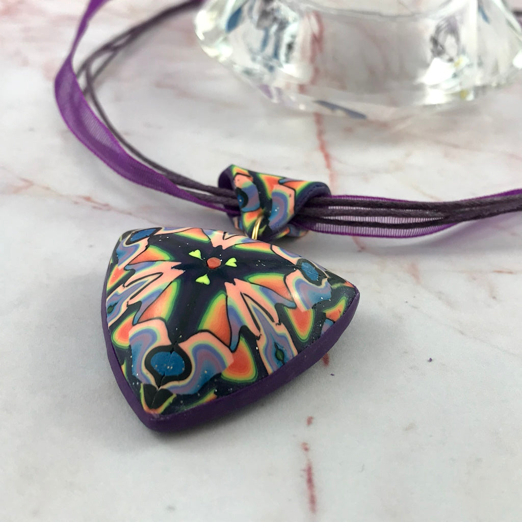 Angled side view of handmade triangular pendant showing depth and sculptural shape.