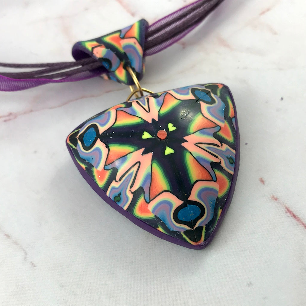 Close-up front view of handmade triangular polymer clay statement pendant in purple and multicolour design.
