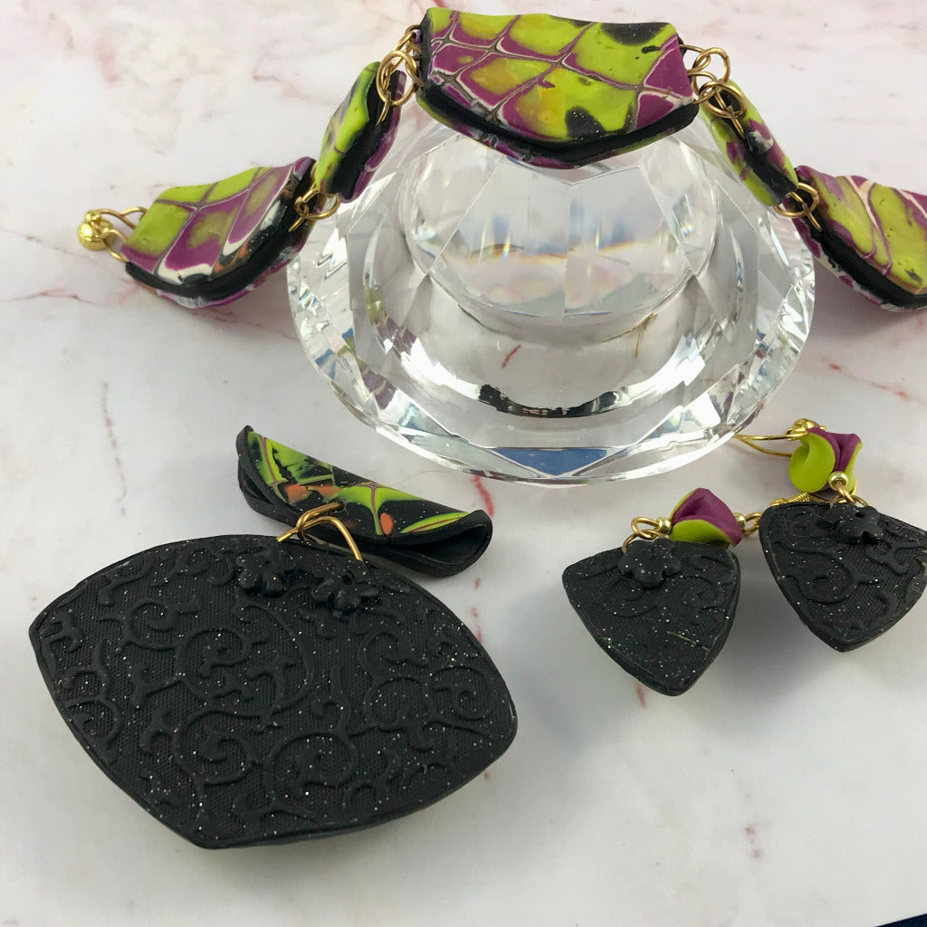 Yellow and purple bracelet displayed on glass with back view of matching pendant and earrings.