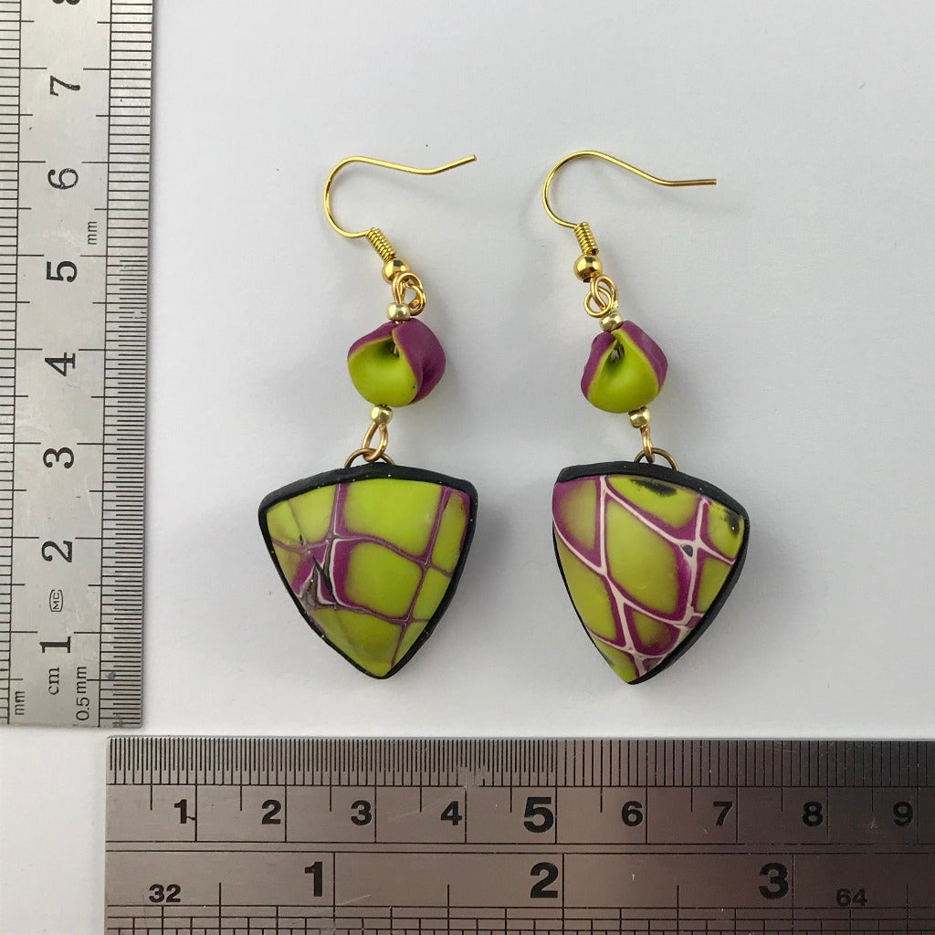 Handmade yellow and purple abstract polymer clay earrings displayed beside a ruler for size reference.