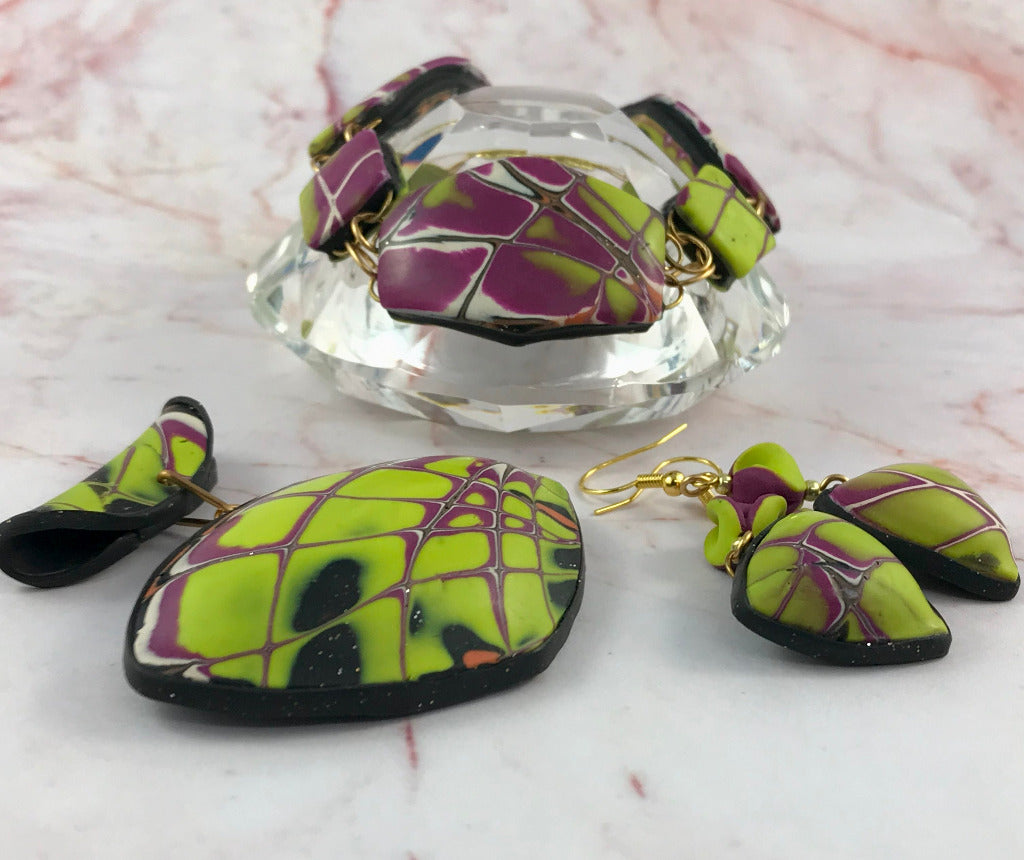 Yellow and purple abstract jewellery set styled beside glass display featuring pendant, bracelet, and earrings.