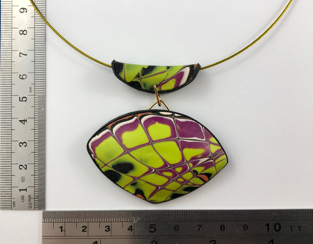 Modern curved yellow and purple polymer clay pendant displayed with ruler for accurate sizing.