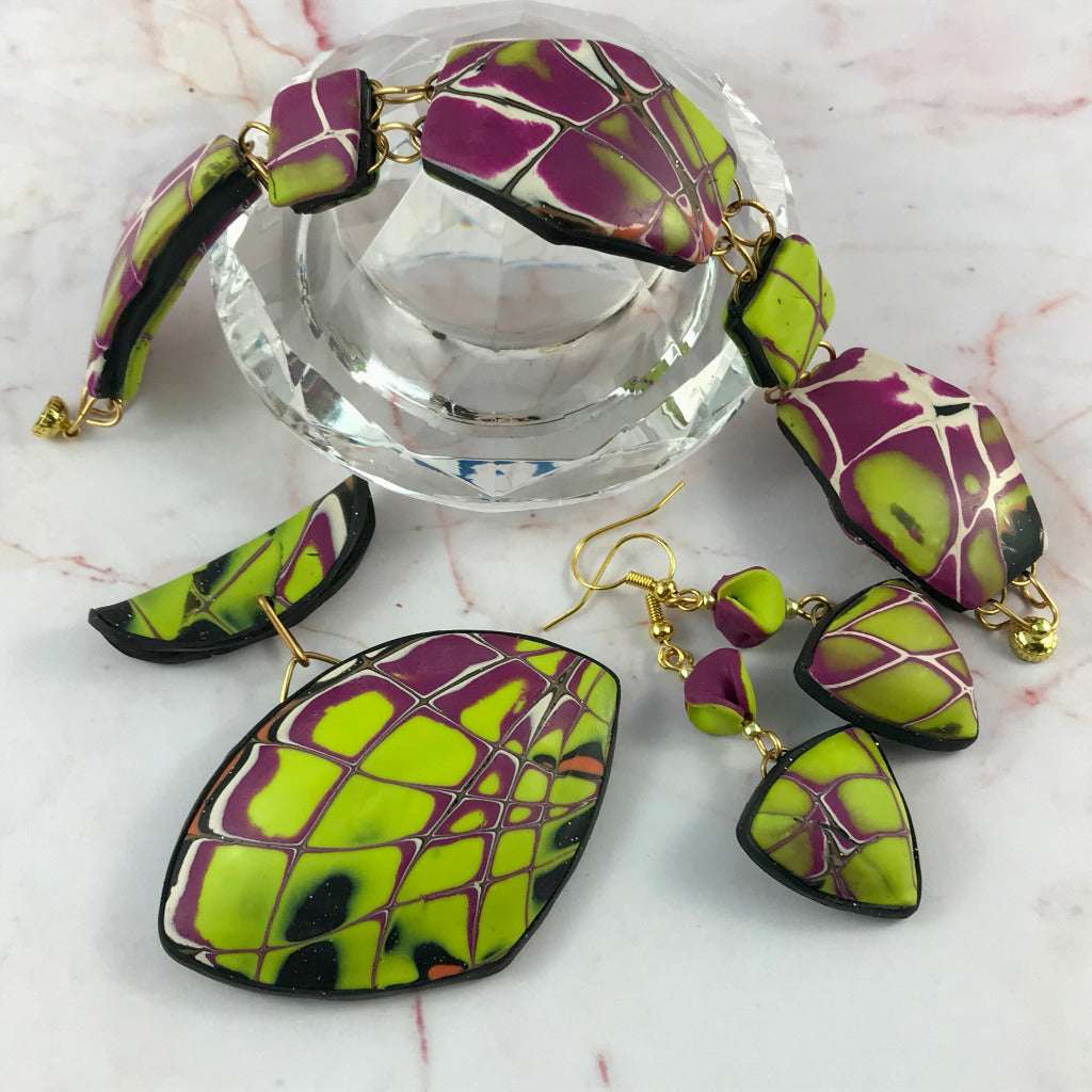 Close-up of yellow and purple polymer clay pendant, bracelet, and earrings on glass surface.