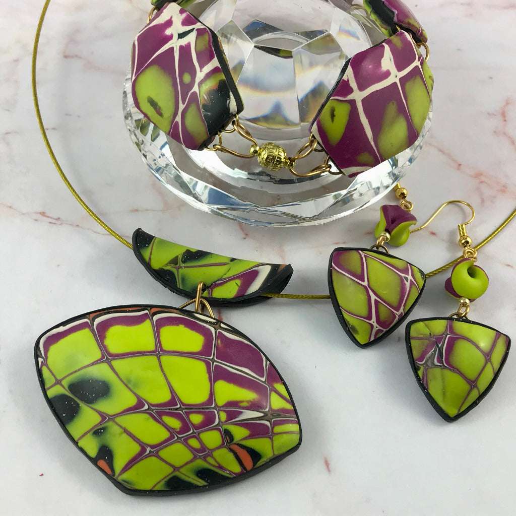 Side profile view of handmade yellow and purple bracelet, pendant, and earrings on glass display.